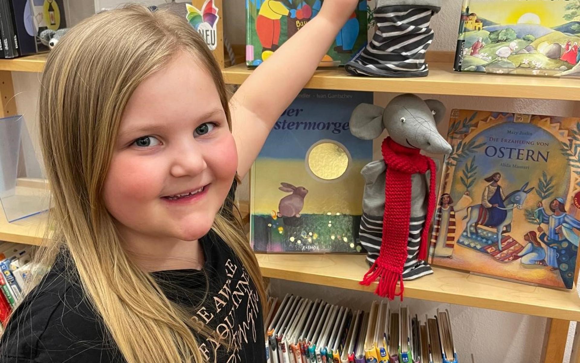 Mädchen mit Handpuppe vor Bücherregal