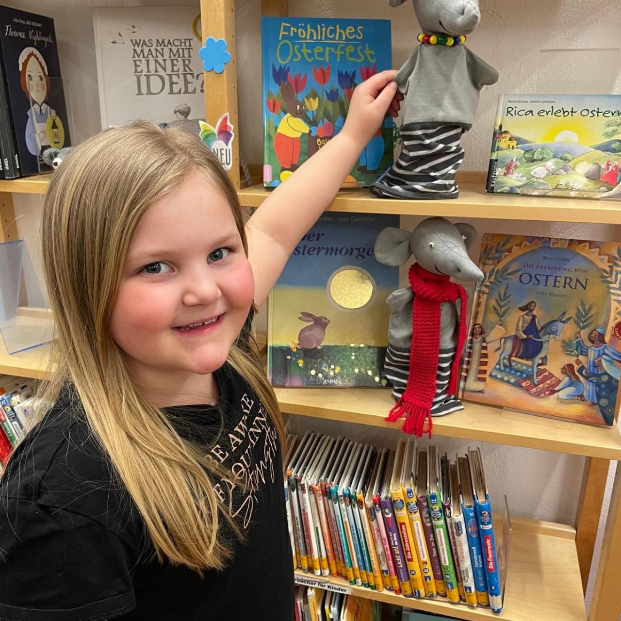 Mädchen mit Handpuppe vor Bücherregal